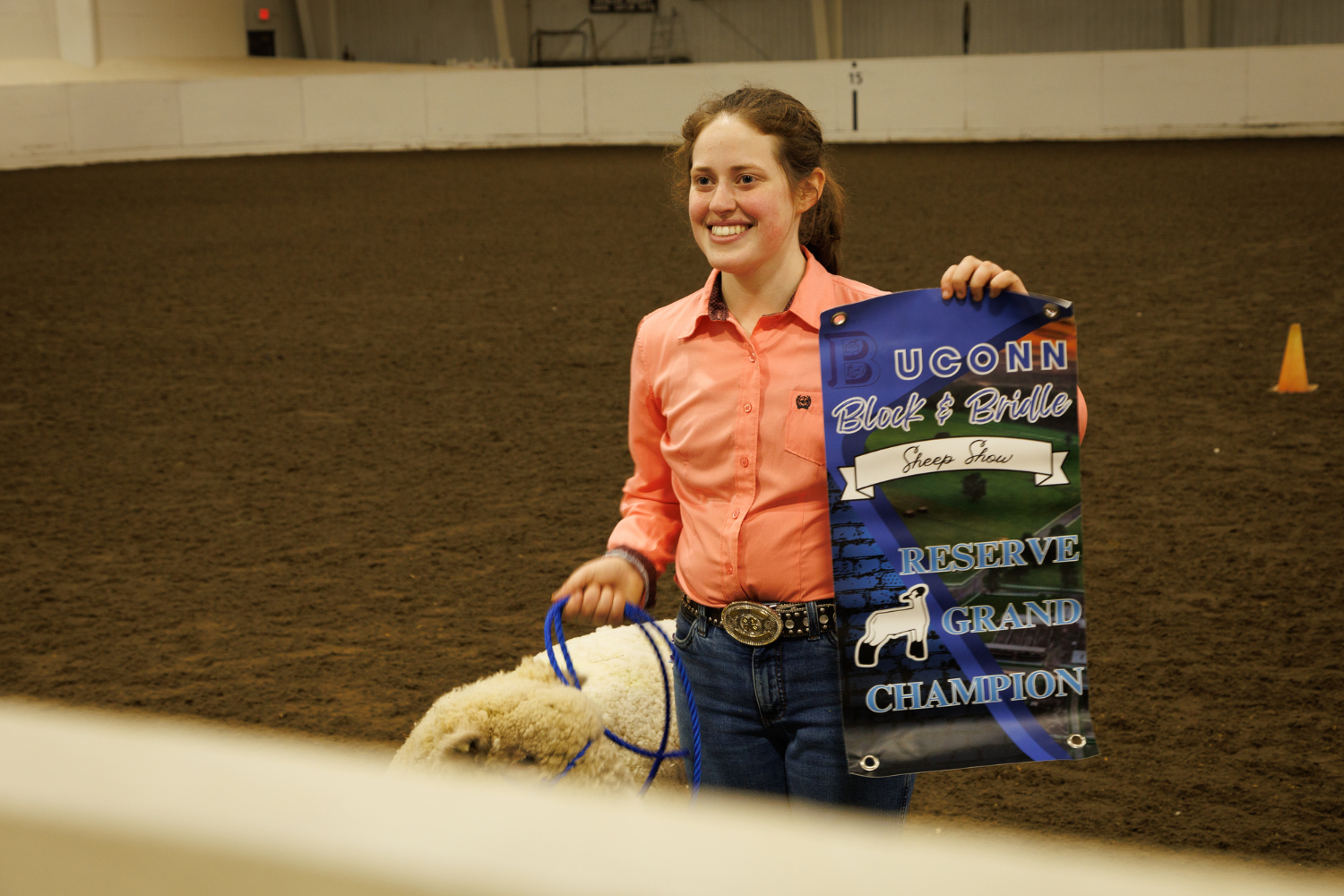 Student posing for photo with their award alongside sheep.